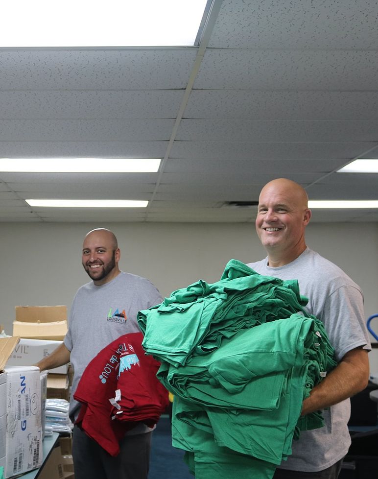two people wearing volunteer shirts holding piles of clothing